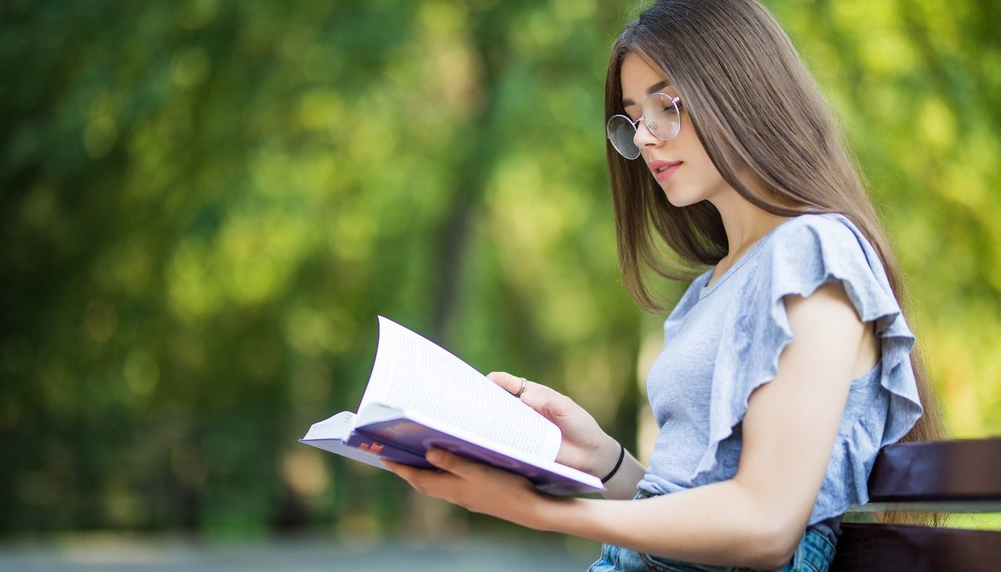 Reading every day. Читает книги за столом вид сбоку. Женщина читает документ обычное фото. Woman student Backside.